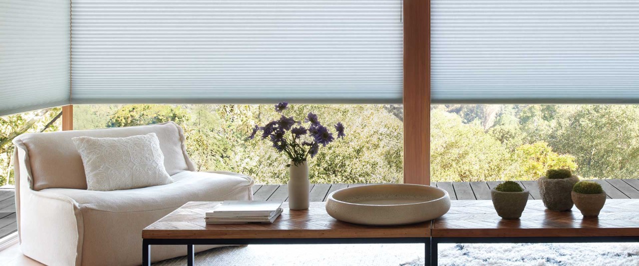 Contemporary living room with long coffee table and flowers overlooking greenery outside.